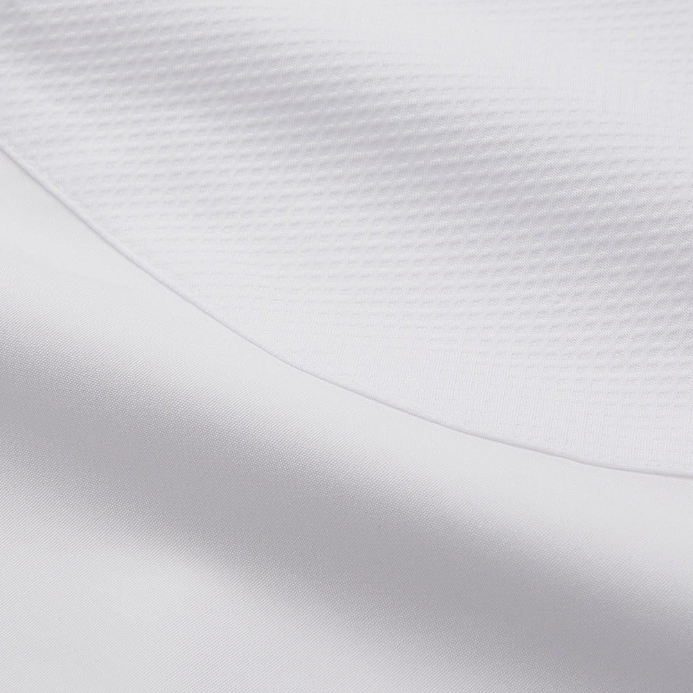 A person with curly hair wears the Turnbull and The Deck White Cotton Minimalist Shirt by Turnbull & Asser, paired with pants. Posed against a plain background, their minimalist silhouette is highlighted in this black and white image.