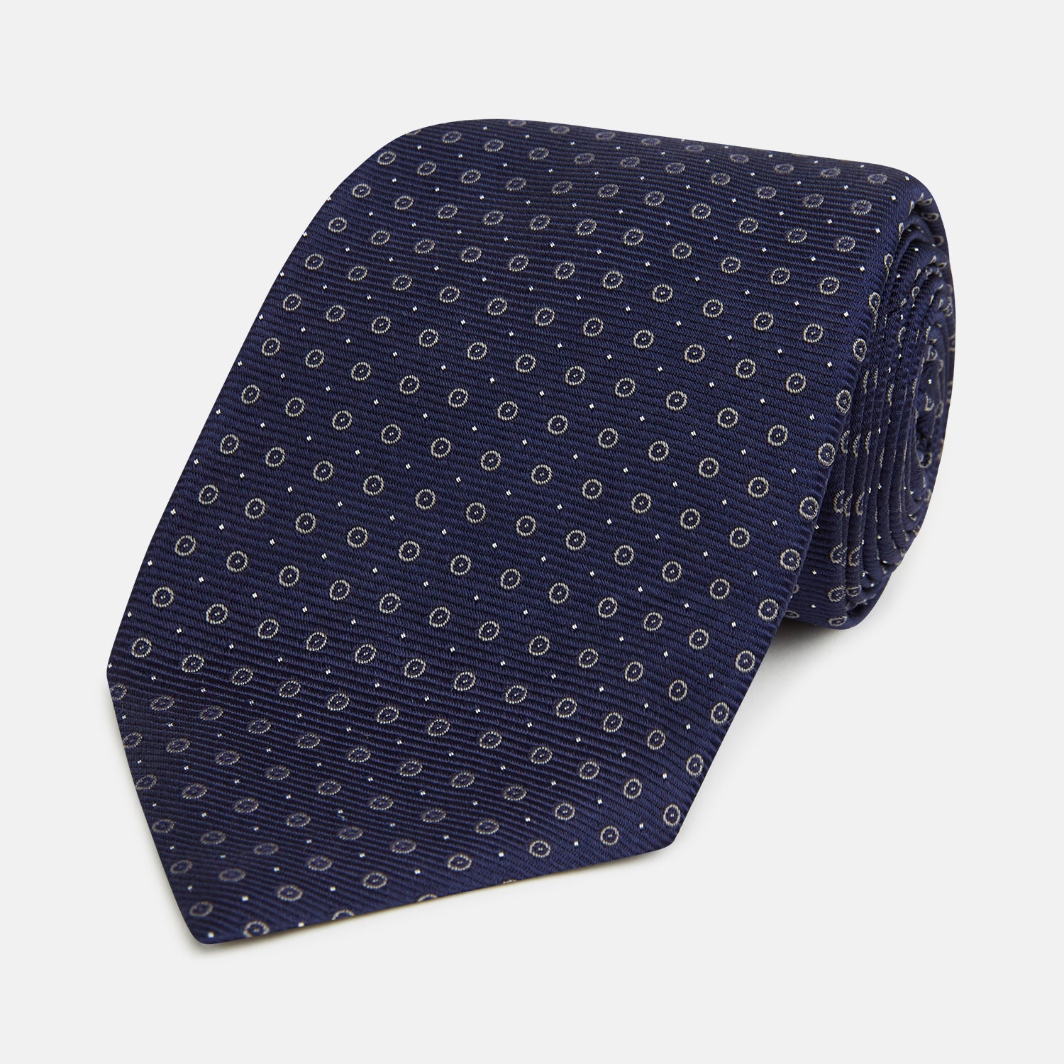 View 1 of product The Turnbull & Asser Navy and Grey Circle Silk Tie, featuring a refined pattern of evenly spaced circles, is elegantly displayed rolled up on a white background—an excellent option for modern office wear.