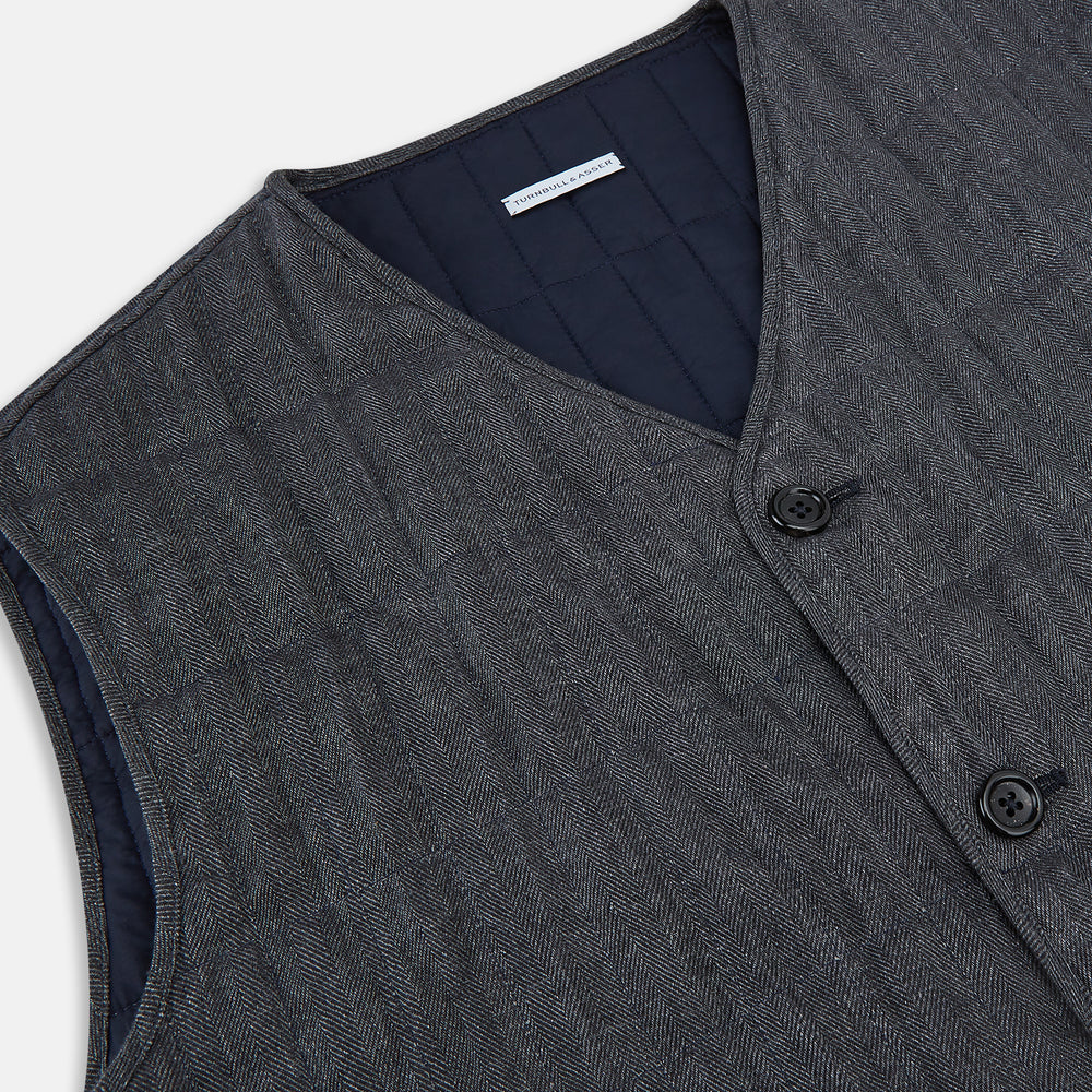 The Turnbull & Asser Ash Quilted Linen Herringbone Waistcoat is sleeveless and dark gray with a V-neck, two zippered side pockets, and a small chest pocket, shown on a plain white background.