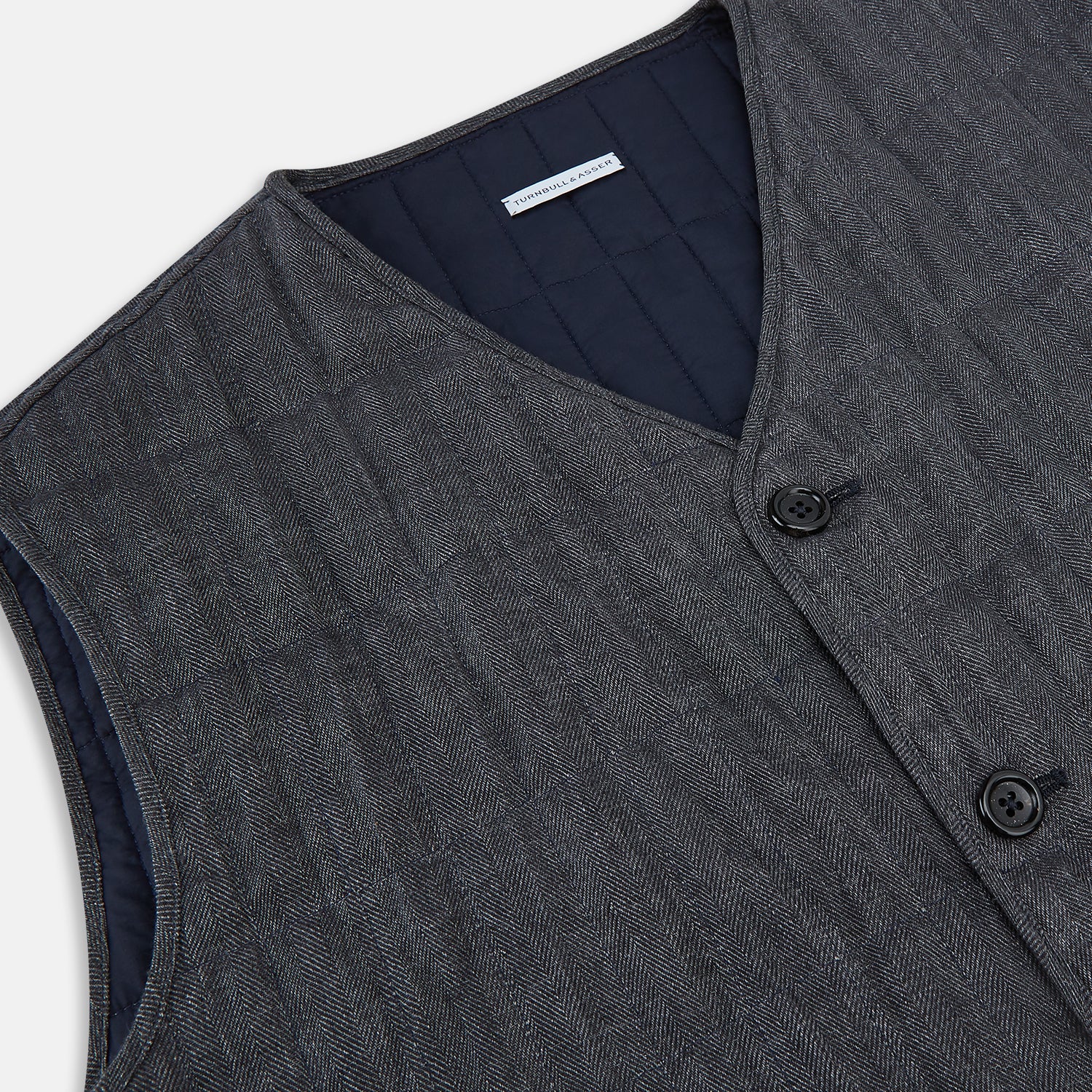 View 2 of product The Turnbull & Asser Ash Quilted Linen Herringbone Waistcoat is sleeveless and dark gray with a V-neck, two zippered side pockets, and a small chest pocket, shown on a plain white background.
