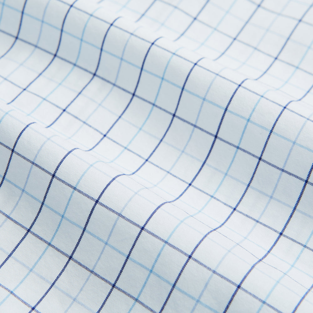 The Blue Overlay Grid Check Mayfair Shirt by Turnbull & Asser features a light blue and white grid check pattern with long sleeves and button-up design, making it a versatile wardrobe staple. Displayed on a plain white background.