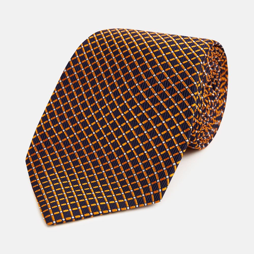 The Turnbull & Asser Orange and Navy Diamond Silk Tie features a yellow and orange diamond pattern on navy silk, ideal for modern office attire, and is displayed rolled up on a light surface.