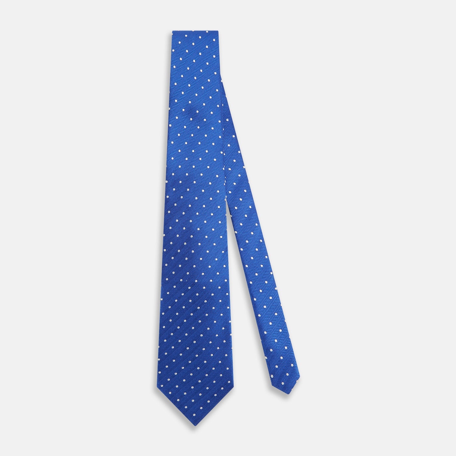 View 2 of product The Turnbull & Asser Blue and White Micro Dot Silk Tie features a subtle herringbone pattern with small white dots, ideal for modern office attire, and is shown rolled up on a white background.