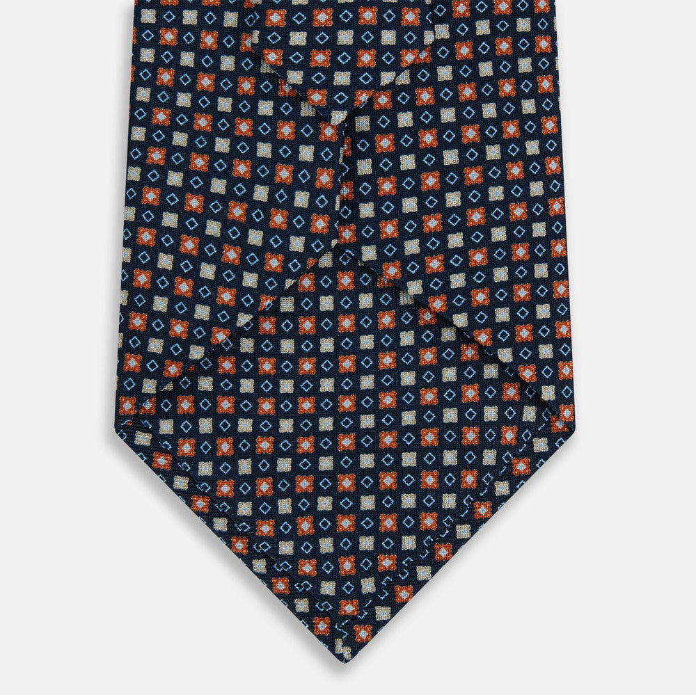 The Turnbull & Asser Navy and Orange Geometric Motif Silk Tie features a dark blue base with small orange, white, and light blue geometric patterns—a refined statement of British craftsmanship.