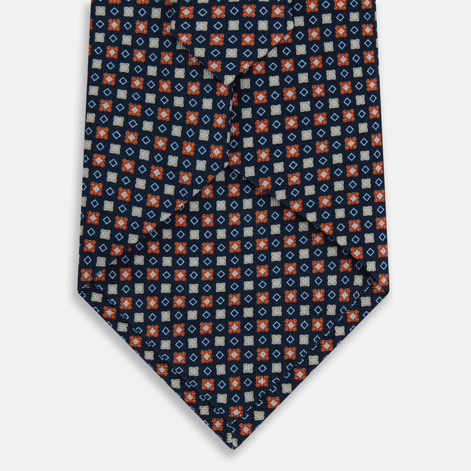 View 3 of product The Turnbull & Asser Navy and Orange Geometric Motif Silk Tie features a dark blue base with small orange, white, and light blue geometric patterns—a refined statement of British craftsmanship.