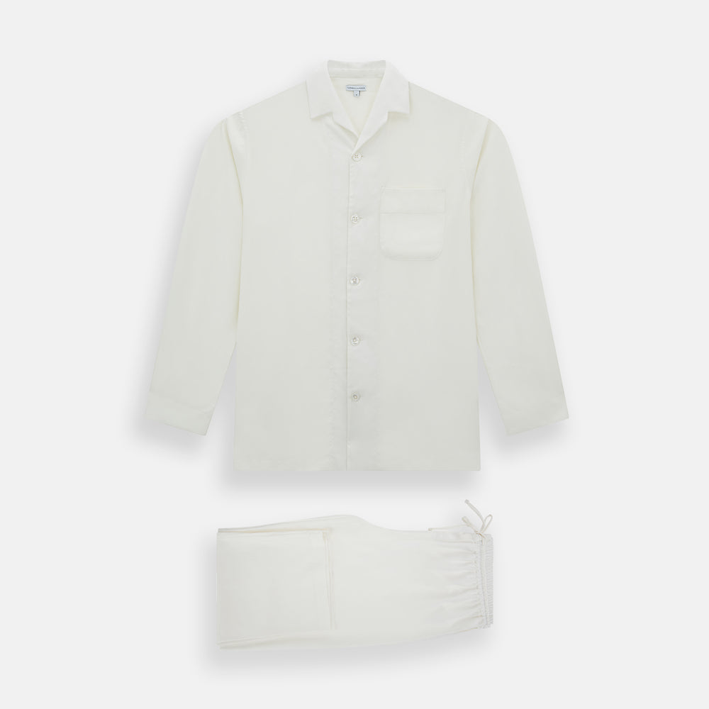 The Turnbull & Asser Cream Silk Pyjama Set, shown laid flat on a white background, features a long-sleeve button-up top with a chest pocket and matching pants with an elastic drawstring waist—ideal for comfortable loungewear.