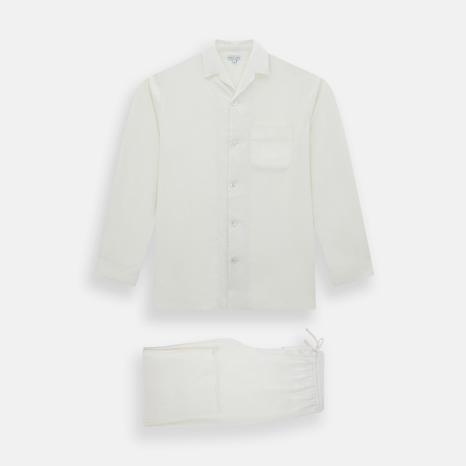 View 1 of product The Turnbull & Asser Cream Silk Pyjama Set, shown laid flat on a white background, features a long-sleeve button-up top with a chest pocket and matching pants with an elastic drawstring waist—ideal for comfortable loungewear.
