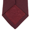 View 4 of product The Turnbull & Asser 7 fold Grenadine Silk Plain Tie is shown rolled on a white background, highlighting its textured maroon design as a versatile addition to any wardrobe.