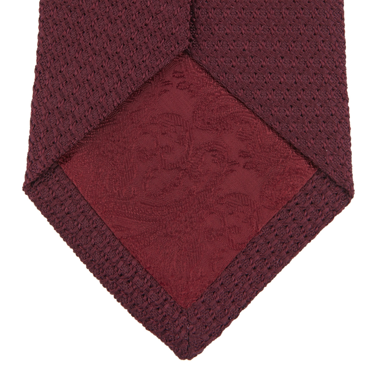 View 4 of product The Turnbull & Asser 7 fold Grenadine Silk Plain Tie is shown rolled on a white background, highlighting its textured maroon design as a versatile addition to any wardrobe.