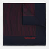 View 1 of product The Turnbull & Asser Navy and Red Stripe Silk Pocket Square features thin red stripes on navy silk, with "HAND PRINTED IN ENGLAND" in red at the corner. A folded corner shows its hand-rolled edges and refined design.