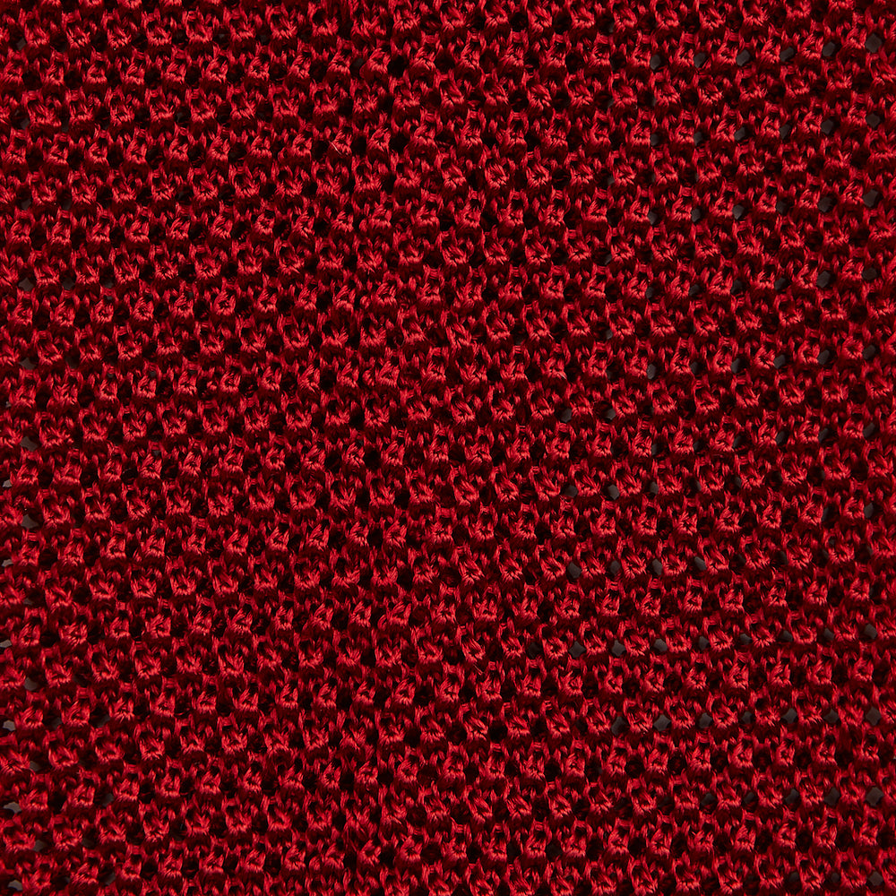 The Turnbull & Asser KNITTED RED SILK PLAIN TIE, featuring a textured finish, is rolled up and displayed against a plain white background.