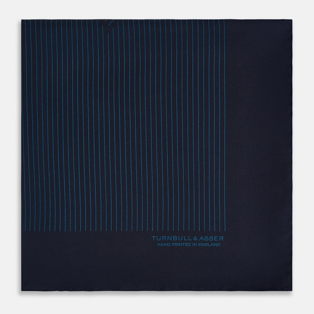 The Navy and Blue Stripe Silk Pocket Square by Turnbull & Asser features vertical blue pinstripes, is crafted from silk with hand-rolled edges, and is finished with the brand's logo printed in blue at the lower right corner.