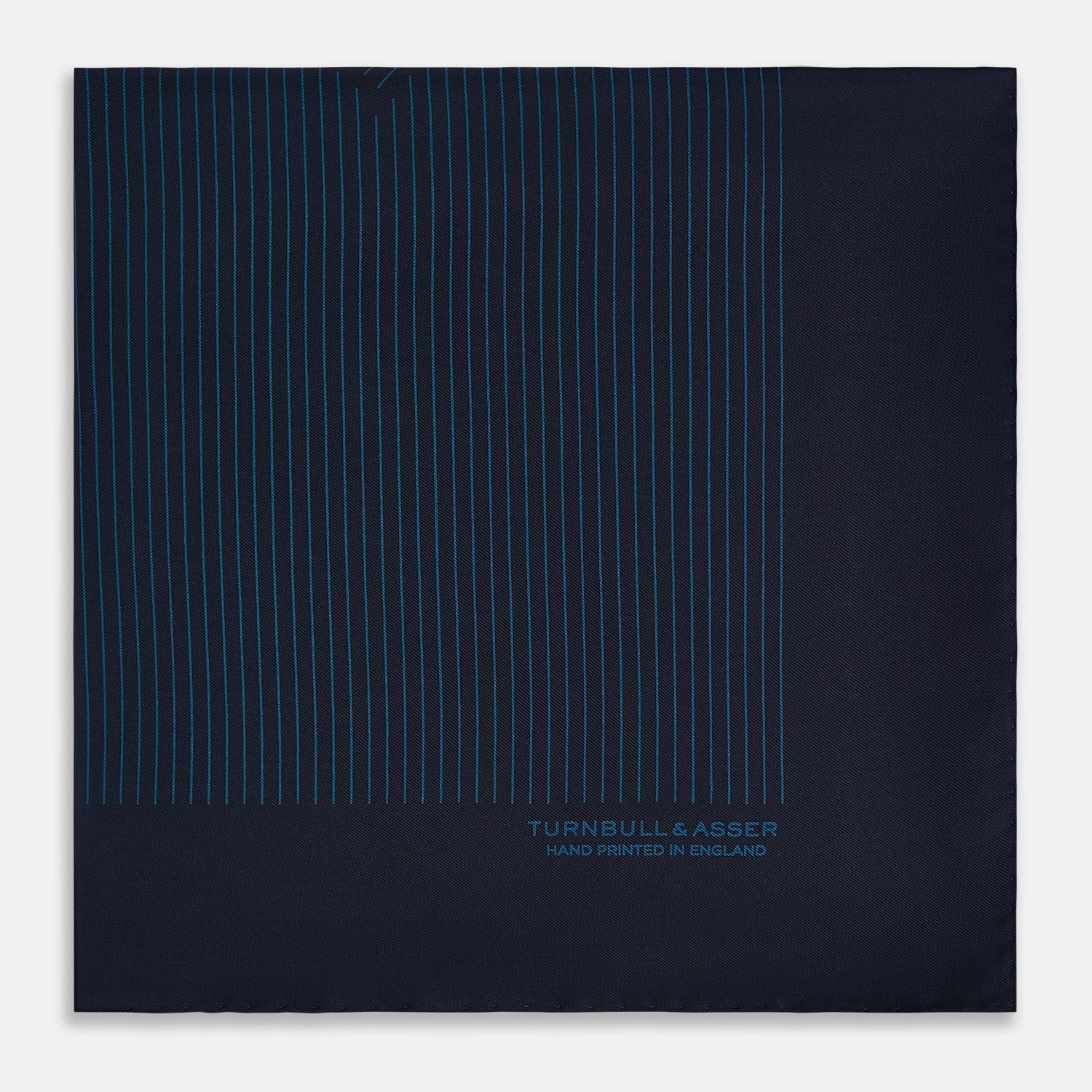 View 4 of product The Navy and Blue Stripe Silk Pocket Square by Turnbull & Asser features vertical blue pinstripes, is crafted from silk with hand-rolled edges, and is finished with the brand's logo printed in blue at the lower right corner.