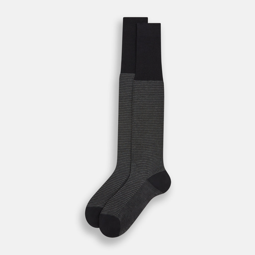 The Turnbull & Asser Charcoal Melange Houndstooth Long Sock is knee-high, with a subtle dark houndstooth pattern and solid black toe, heel, and cuff, shown on a white background.