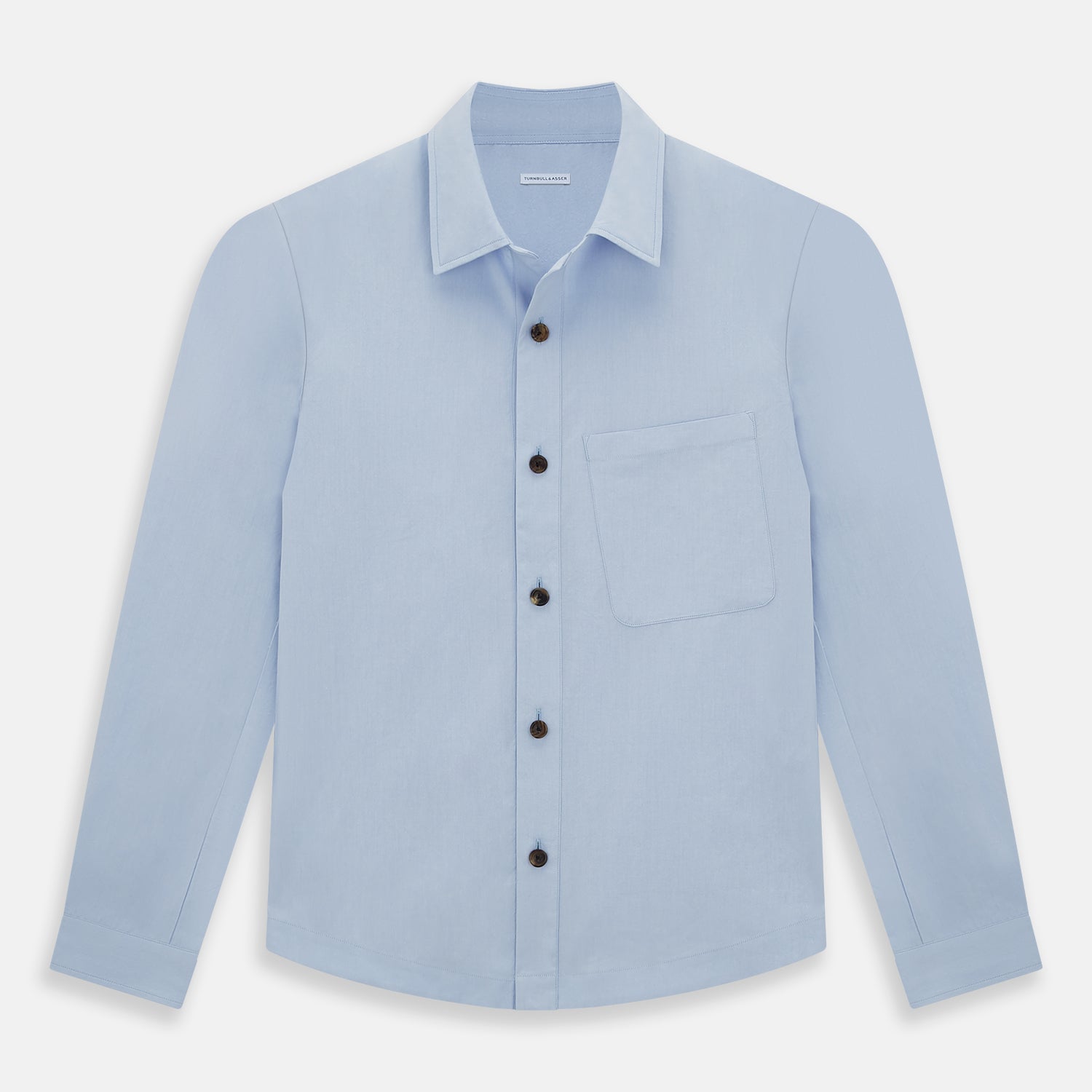 View 1 of product The Turnbull & Asser Pale Blue Hyde Overshirt is a long-sleeve, sanforised cotton button-up with a single chest pocket and dark buttons, shown on a plain white background.