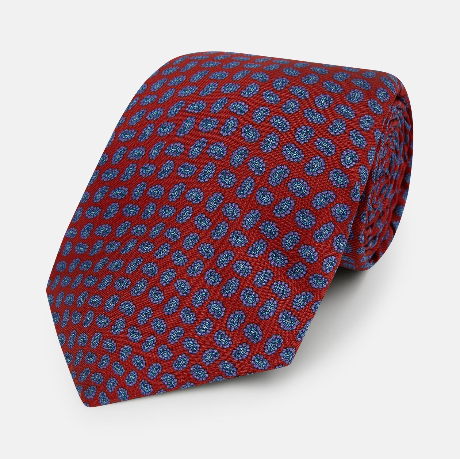 View 1 of product The Turnbull & Asser Red and Purple Miniature Paisley Silk Tie is neatly rolled with the pointed end facing forward.