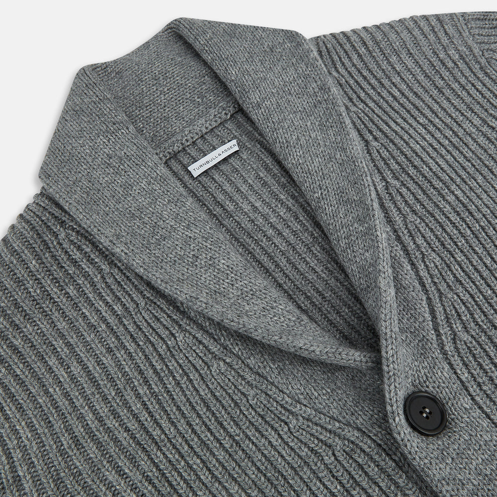 The Turnbull & Asser Grey Melange Cashmere Shawl Collar Cardigan features a ribbed-knit texture, five black front buttons, and two pockets, shown against a plain white background.