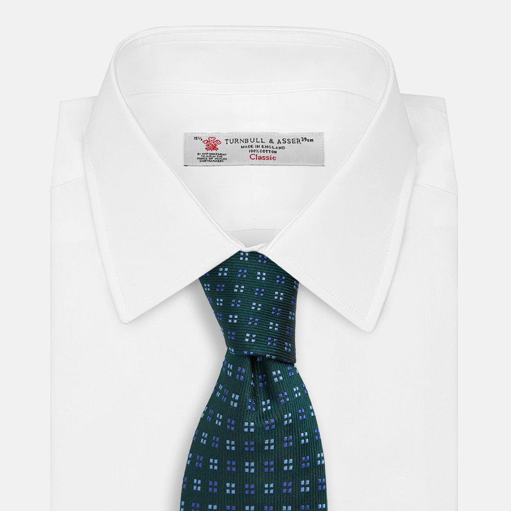 The MINI SQUARE SPOT FOREST GREEN BLUE TIE by Turnbull & Asser is a classic men's accessory, featuring a rolled-up green silk design with small blue geometric patterns—perfect for the modern gentleman.