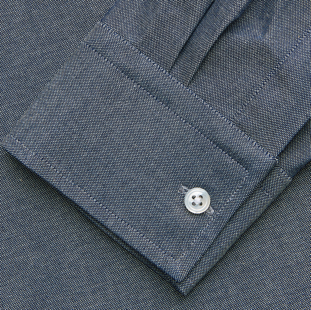 The Turnbull & Asser Plain Blue Oxford Cotton Weekend Fit Blake Shirt features long sleeves, a stand collar, and white buttons, displayed flat on a white background.
