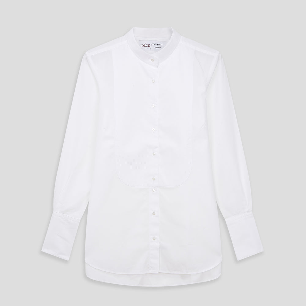 A person with curly hair wears the Turnbull and The Deck White Cotton Minimalist Shirt by Turnbull & Asser, paired with pants. Posed against a plain background, their minimalist silhouette is highlighted in this black and white image.