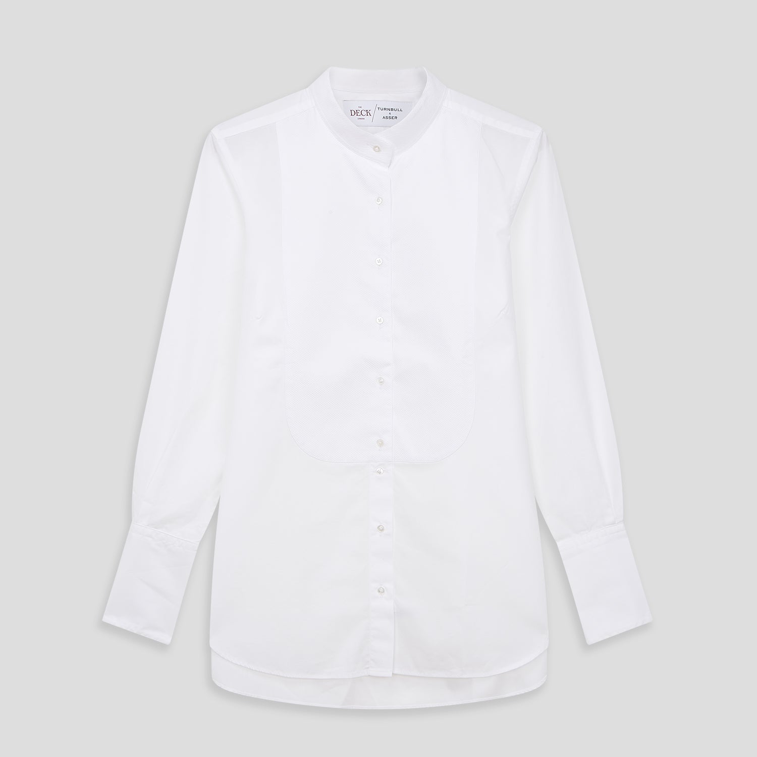 View 2 of product A person with curly hair wears the Turnbull and The Deck White Cotton Minimalist Shirt by Turnbull & Asser, paired with pants. Posed against a plain background, their minimalist silhouette is highlighted in this black and white image.