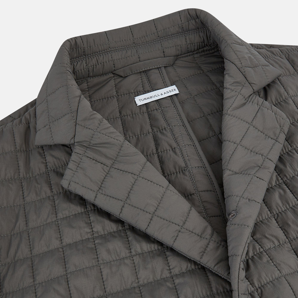 The Fulham Shadow Grey Single-Breasted Quilted Blazer by Turnbull & Asser features a checkered pattern, notched lapel, three front buttons, chest pocket, and two flap pockets—ideal for formal wear on a plain white background.