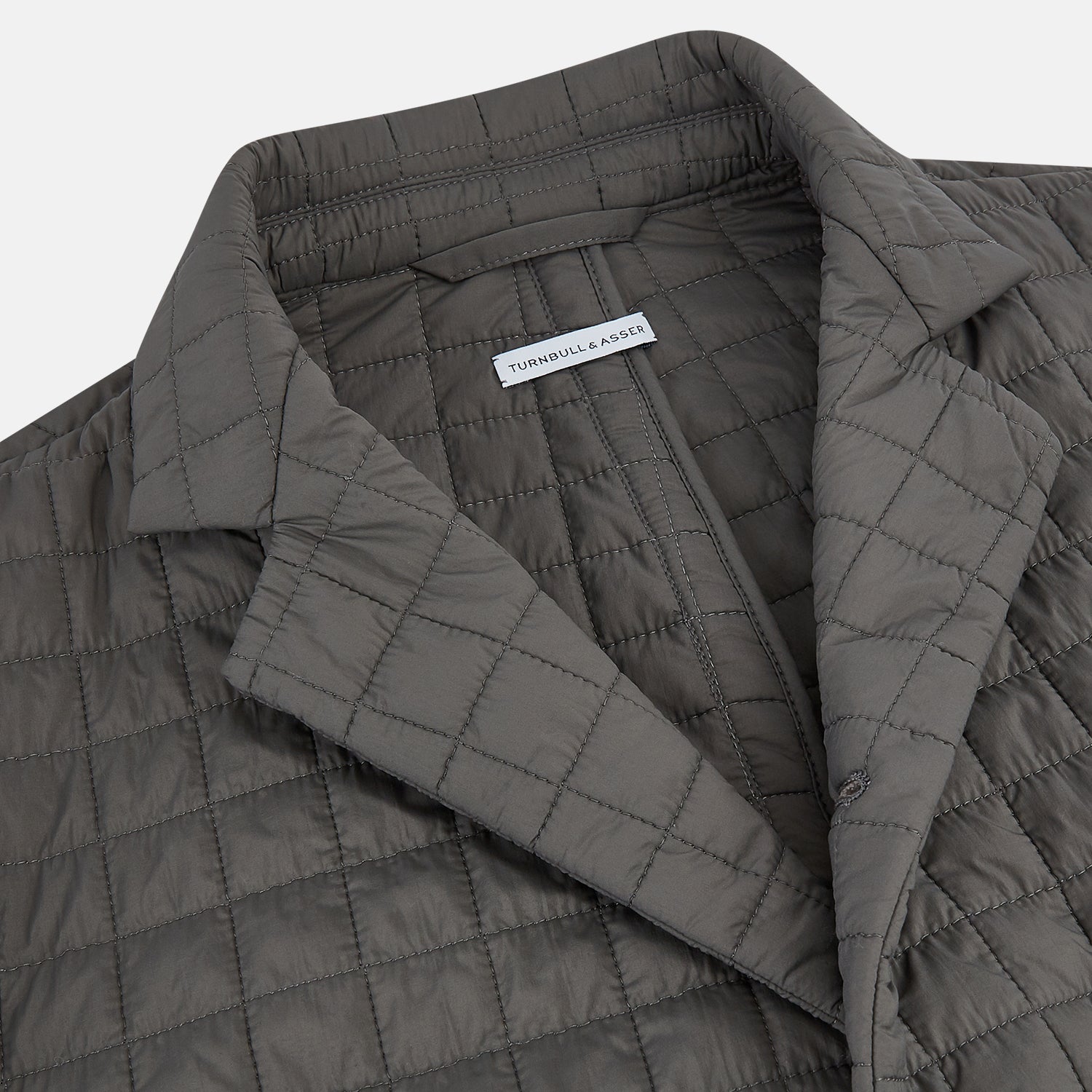 View 2 of product The Fulham Shadow Grey Single-Breasted Quilted Blazer by Turnbull & Asser features a checkered pattern, notched lapel, three front buttons, chest pocket, and two flap pockets—ideal for formal wear on a plain white background.