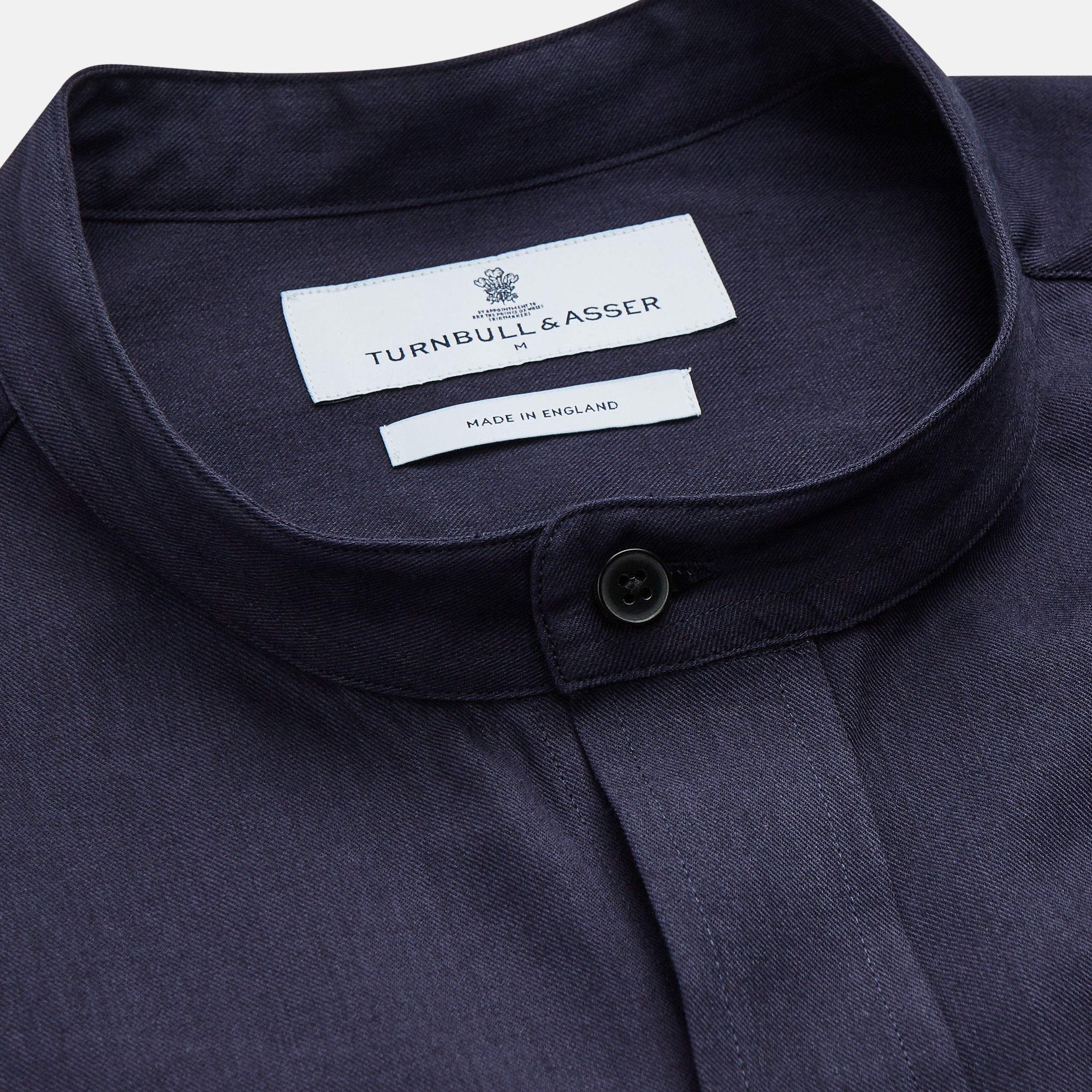 View 2 of product The Turnbull & Asser Navy Military Weekend Fit Shirt features a stand collar, black buttons, dual chest flap pockets, and 1-button cuffs in Italian cotton-wool, shown laid flat on a white background.
