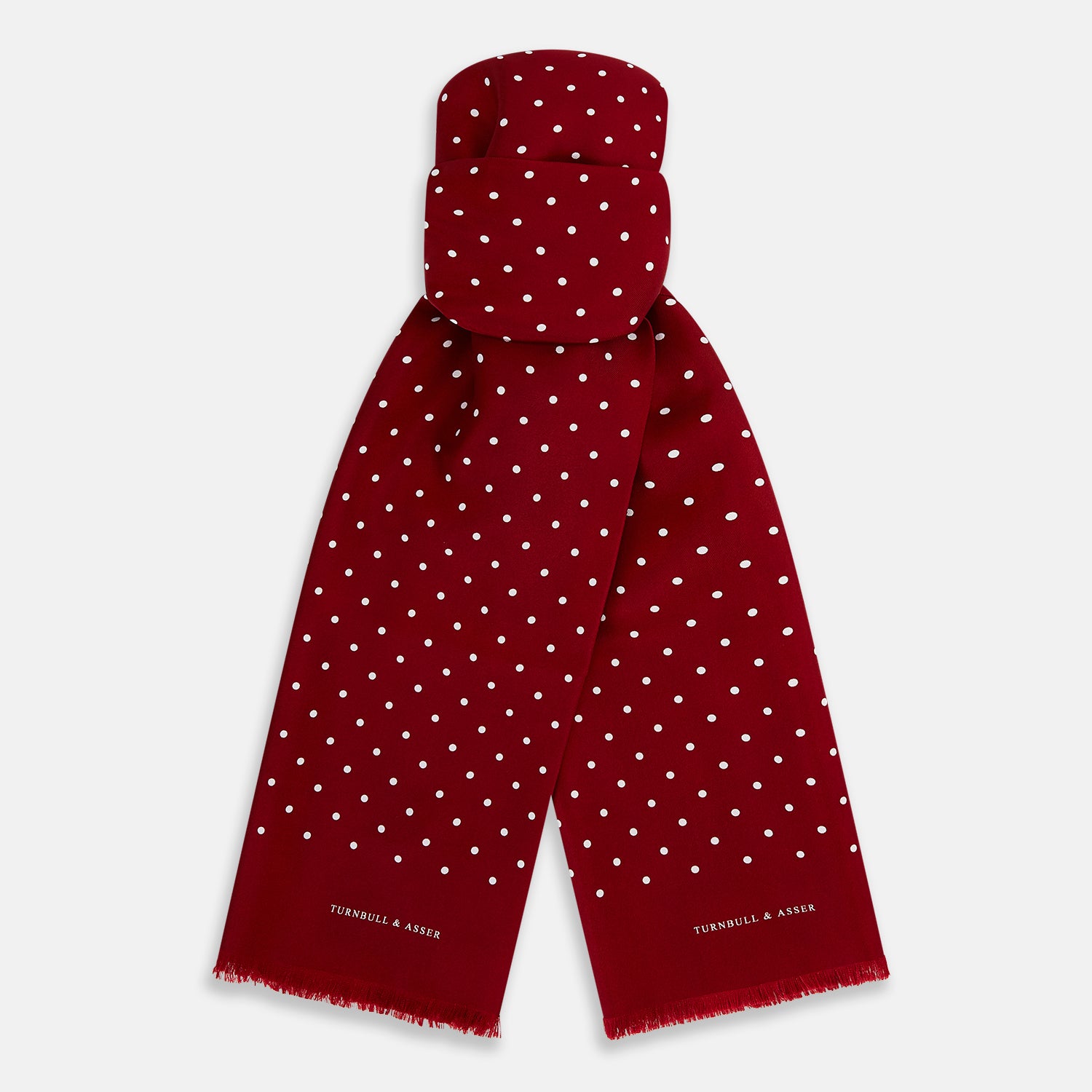 View 1 of product The Burgundy and White Spotted Silk Scarf by Turnbull & Asser features a gradient of white polka dots, short fringed edges, and the brand's name near the ends—a timeless classic foulard.