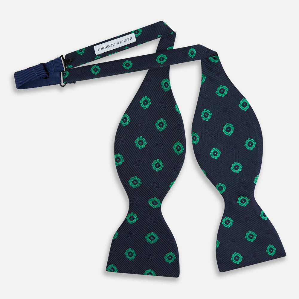 The Navy and Green Motif Silk Bow Tie by Turnbull & Asser features geometric floral patterns, ideal for formalwear, and is shown on a white background.