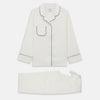 View 2 of product The Women's Harriet Cream Silk Pyjama Set by Turnbull & Asser features a white sand-washed silk button-up top with black piping and chest pocket, plus matching drawstring pants, all shown against a white background.