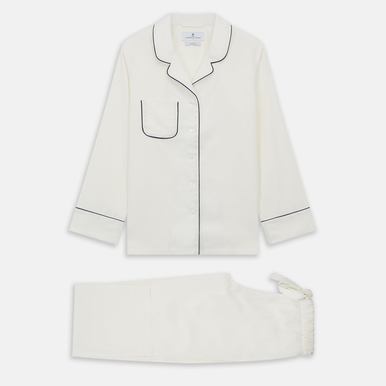 View 2 of product The Women's Harriet Cream Silk Pyjama Set by Turnbull & Asser features a white sand-washed silk button-up top with black piping and chest pocket, plus matching drawstring pants, all shown against a white background.