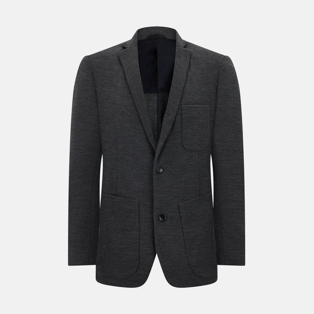 The Turnbull & Asser Graphite Knitted Oxford Blazer for men features a dark gray hue, two buttons, notched lapels, and three front pockets—a modern British-inspired piece styled elegantly against a light background.