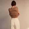 View 4 of product A woman stands barefoot indoors against a neutral wall, wearing Turnbull & Asser Women's Cream Cashmere Knitted Tabitha Bottoms and a light brown sweater. Soft sunlight casts a gentle shadow on the wall beside her.