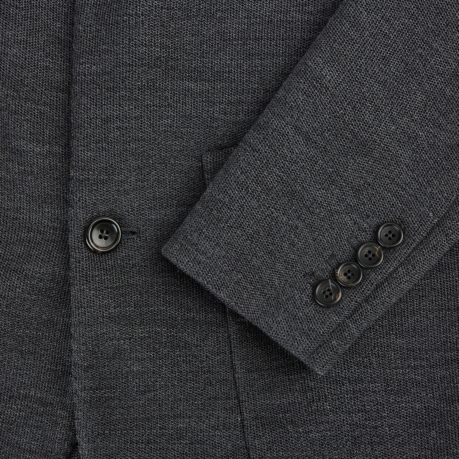 View 4 of product The Turnbull & Asser Graphite Knitted Oxford Blazer for men features a dark gray hue, two buttons, notched lapels, and three front pockets—a modern British-inspired piece styled elegantly against a light background.