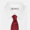 View 2 of product The HORIZONTAL TWILL BURGUNDY TIE by Turnbull & Asser features a subtle textured pattern in solid burgundy, rolled neatly and displayed against a white background—a versatile addition to any gentleman’s wardrobe.