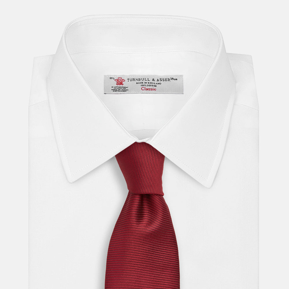 The HORIZONTAL TWILL BURGUNDY TIE by Turnbull & Asser features a subtle textured pattern in solid burgundy, rolled neatly and displayed against a white background—a versatile addition to any gentleman’s wardrobe.