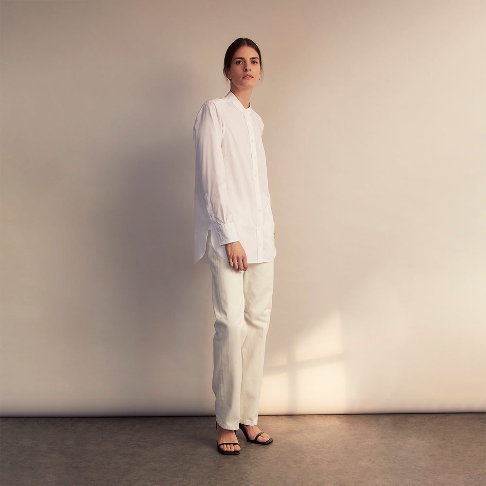 The White Cotton Lauren Shirt by Turnbull & Asser, featuring a stand collar, button-down front, and elongated body, is laid flat on a plain white background.
