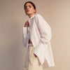 View 3 of product A woman with straight brown hair pulled back wears the Turnbull & Asser White Cotton Marlene Shirt, featuring classic menswear details, paired with high-waisted cream trousers against a neutral background.