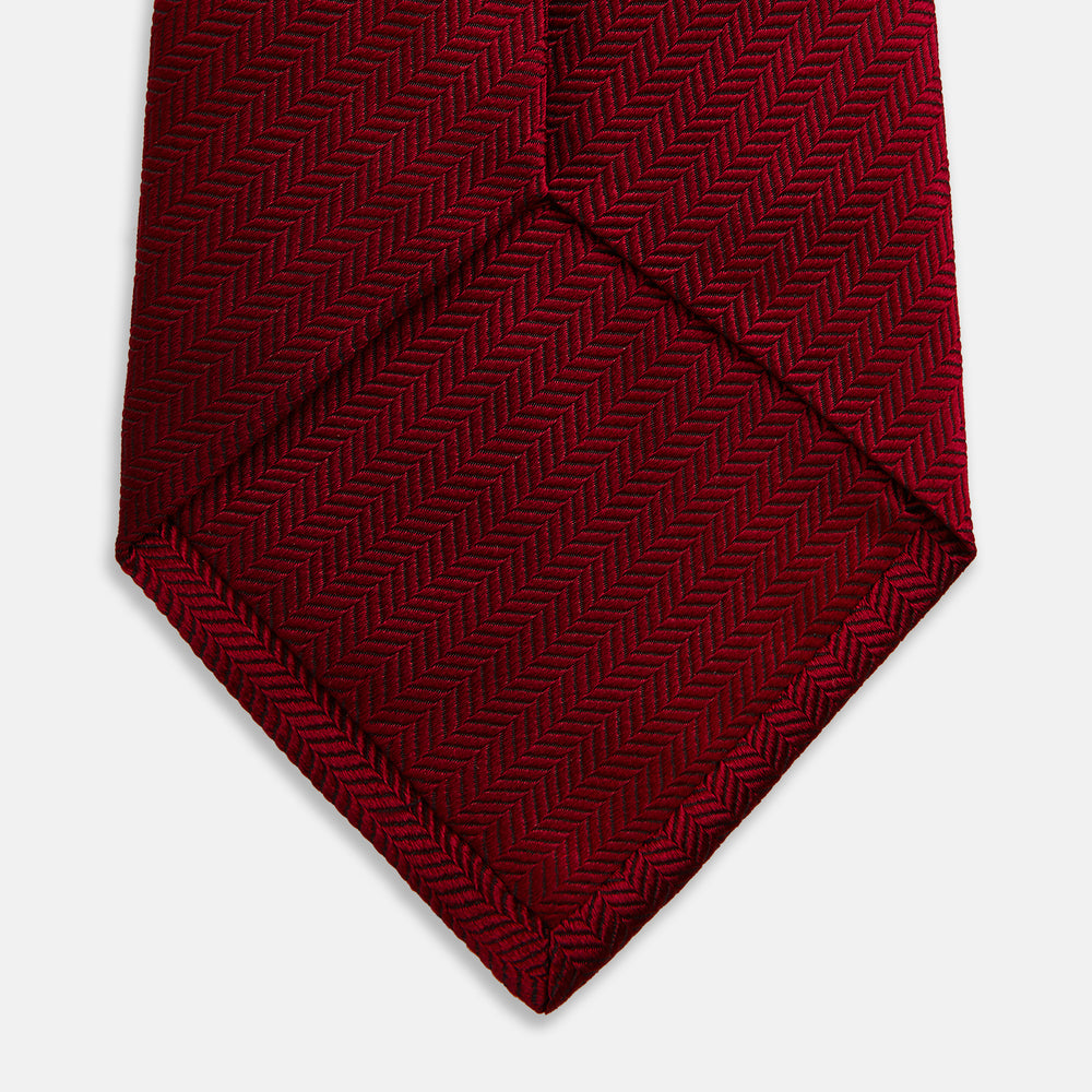 The Turnbull & Asser Plain Herringbone Burgundy Tie features a subtle pattern and rich color, making it an essential accessory for smart attire. Neatly rolled, it’s elegantly displayed on a plain white background.