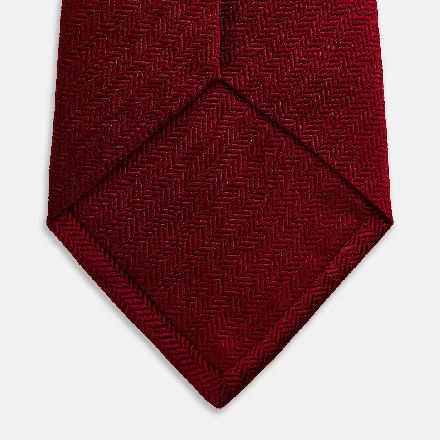 View 4 of product The Turnbull & Asser Plain Herringbone Burgundy Tie features a subtle pattern and rich color, making it an essential accessory for smart attire. Neatly rolled, it’s elegantly displayed on a plain white background.