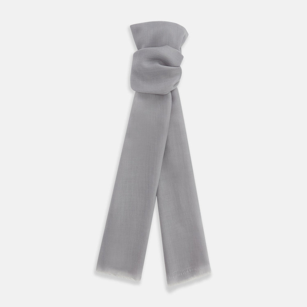 The Grey Cashmere Scarf by Turnbull & Asser, displayed folded with a loose knot on a white background, showcases semi-sheer luxury in light gray—an elegant accessory.