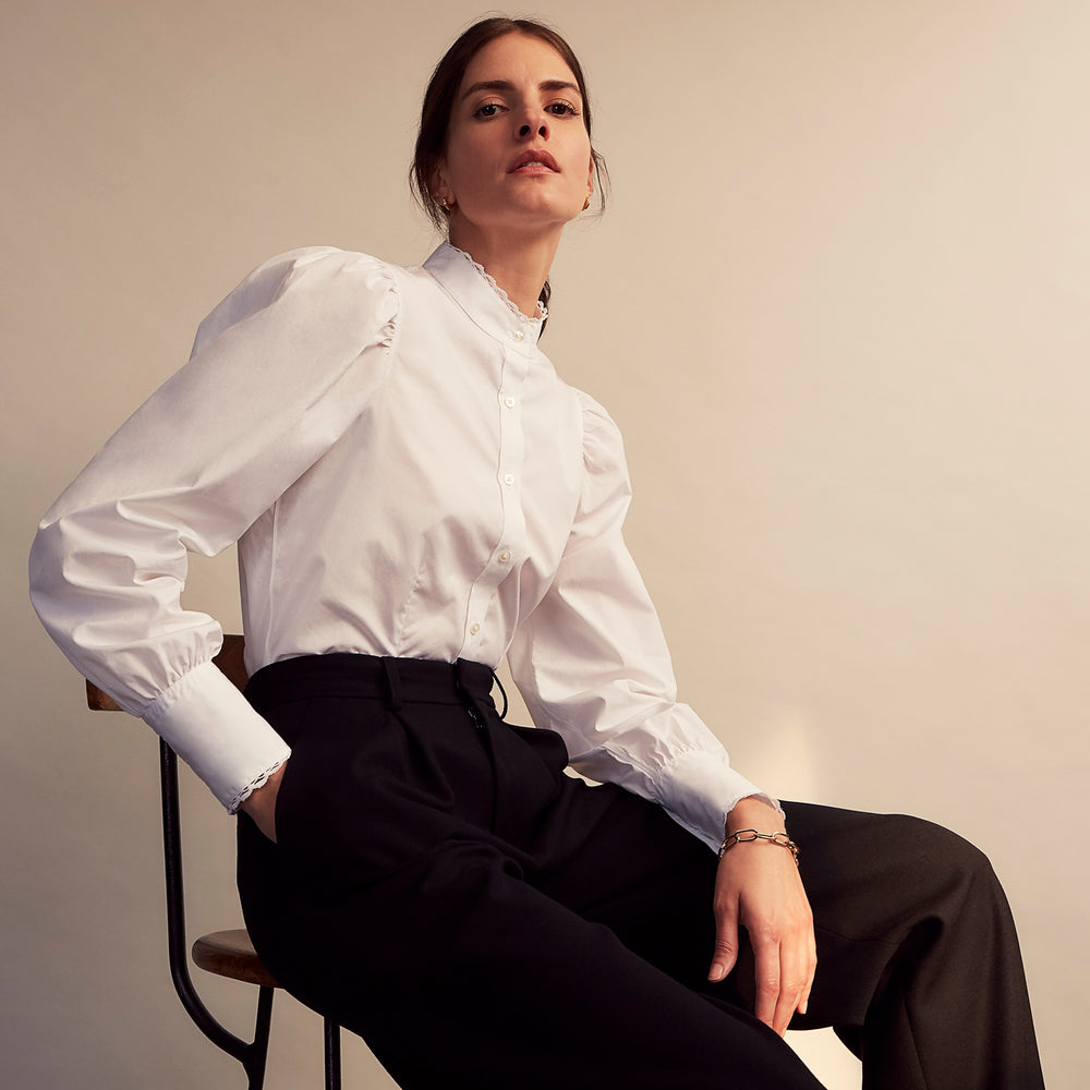 A woman stands in profile, looking down with hands in her pockets, wearing the Turnbull & Asser Turnbull and The Deck White Cotton Expressionist Shirt, paired with high-waisted black-and-white houndstooth pants.