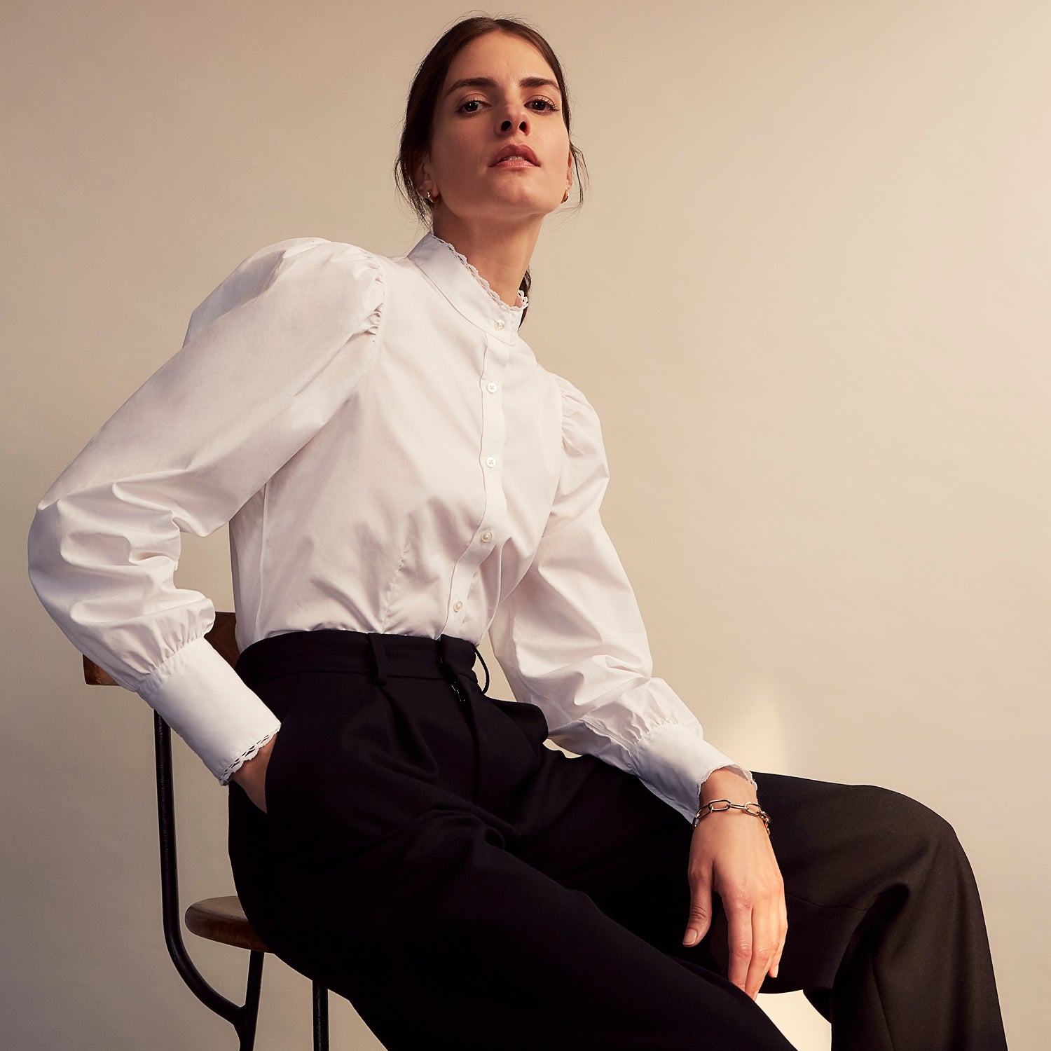 View 9 of product A woman stands in profile, looking down with hands in her pockets, wearing the Turnbull & Asser Turnbull and The Deck White Cotton Expressionist Shirt, paired with high-waisted black-and-white houndstooth pants.
