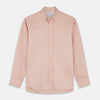View 2 of product A man faces forward in a relaxed pose against a beige background, wearing the Turnbull & Asser Pink Piece Dyed Weekend Fit Suffolk Shirt with a button-down collar, dark cuffed jeans, and black shoes.