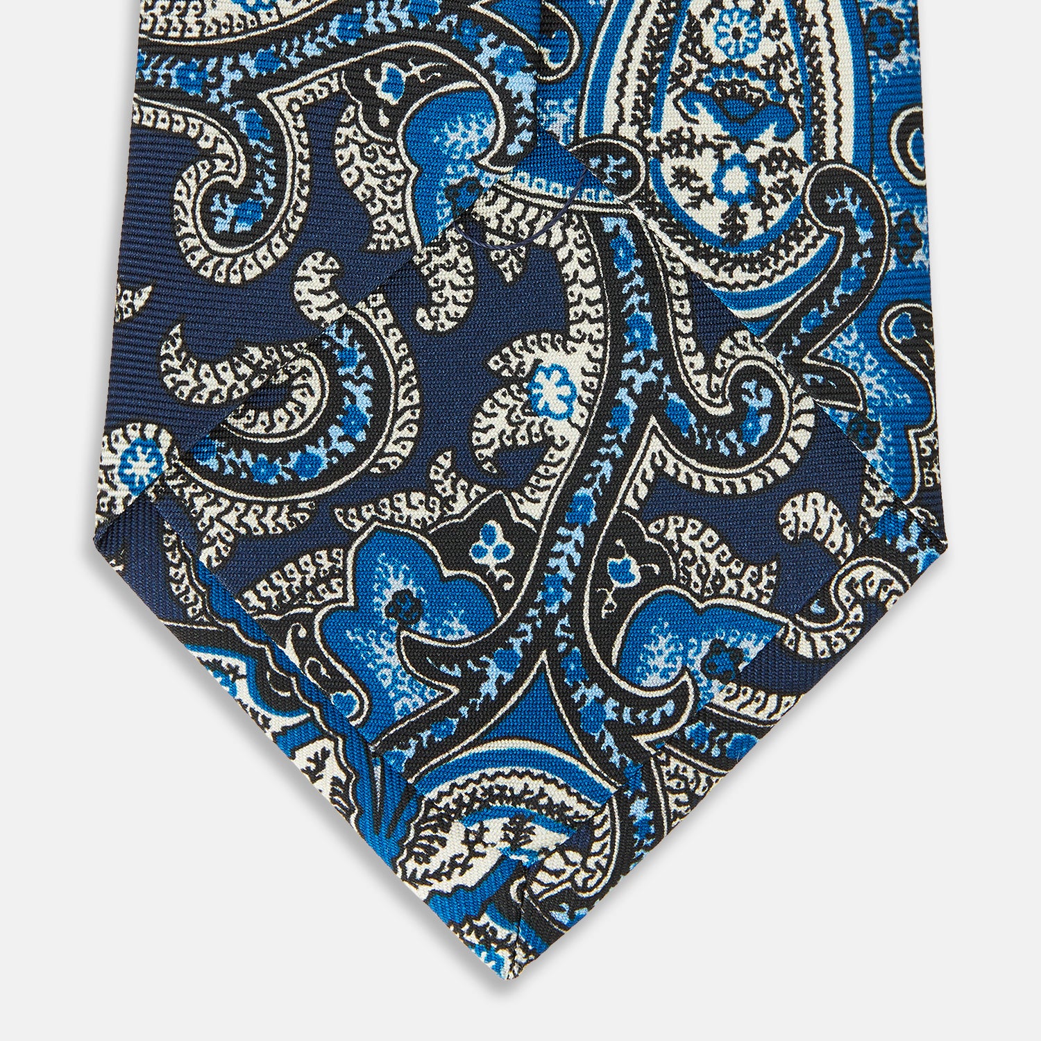 View 4 of product The Turnbull & Asser Blue and Navy Twisted Paisley Silk Tie displays intricate blue, white, and black details, rolled up against a plain white background.