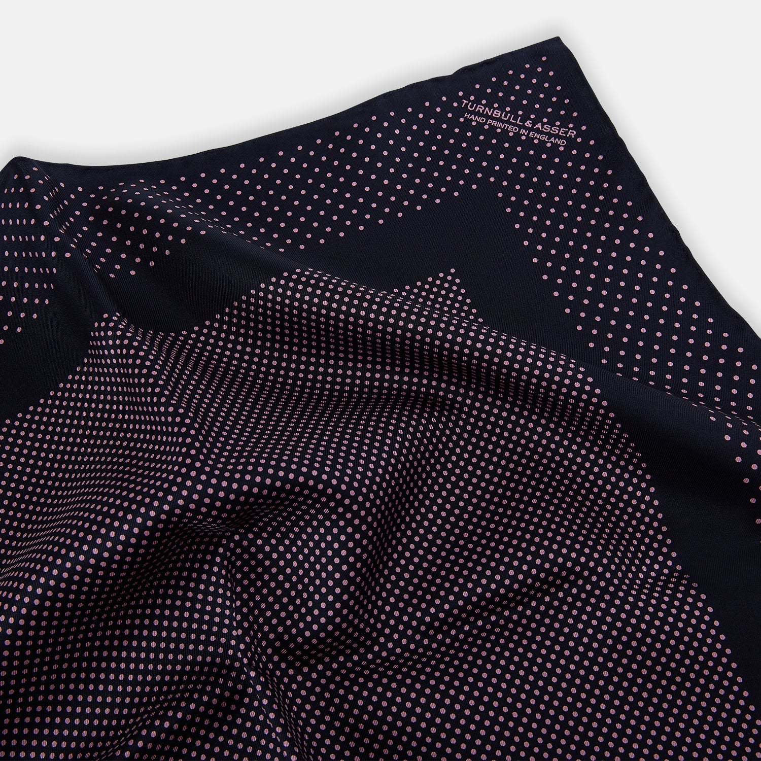 View 2 of product The Turnbull & Asser Navy and Pink Dot Silk Pocket Square features small pink dots and a solid border, with one corner folded to display both sides—an elegant accessory that reflects fine handmade craftsmanship.