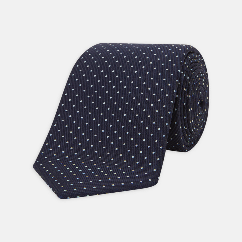 The Turnbull & Asser White and Navy Spot Printed Silk Tie, shown rolled with its pointed end forward on a white background, is an elegant accessory that pairs perfectly with a crisp shirt for smart occasions.