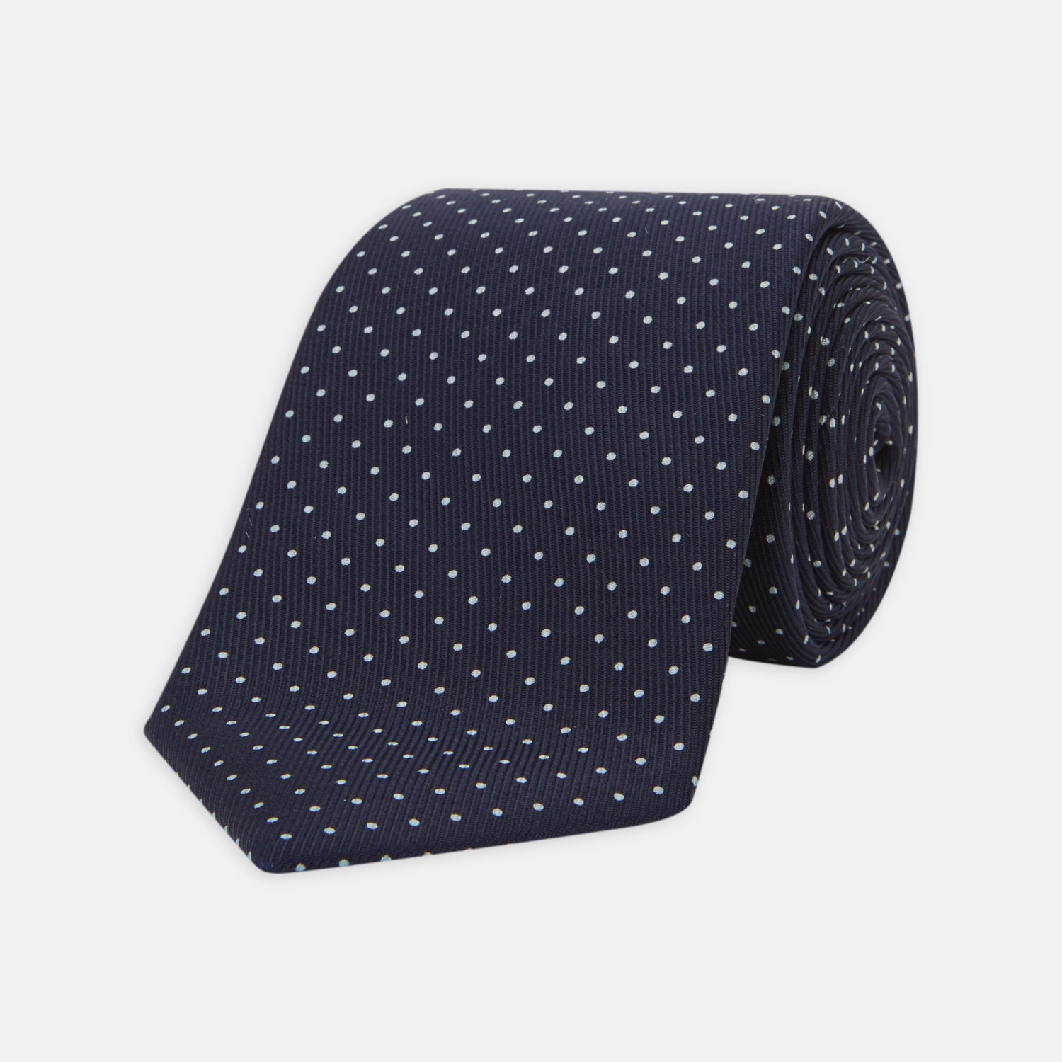 View 1 of product The Turnbull & Asser White and Navy Spot Printed Silk Tie, shown rolled with its pointed end forward on a white background, is an elegant accessory that pairs perfectly with a crisp shirt for smart occasions.
