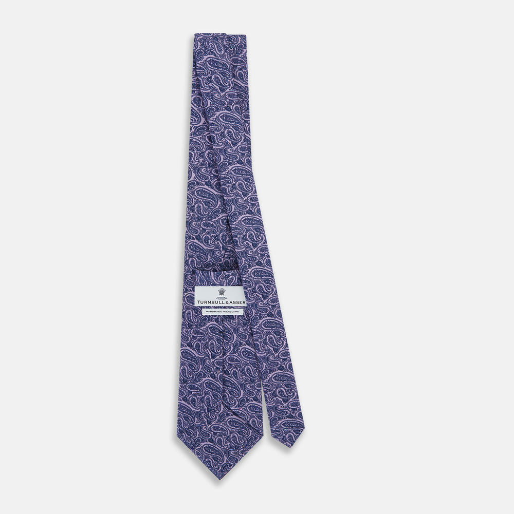 The Turnbull & Asser Lilac Paisley Silk Tie, crafted in England, features a blue paisley pattern on a lilac background and is shown rolled up against a white surface.
